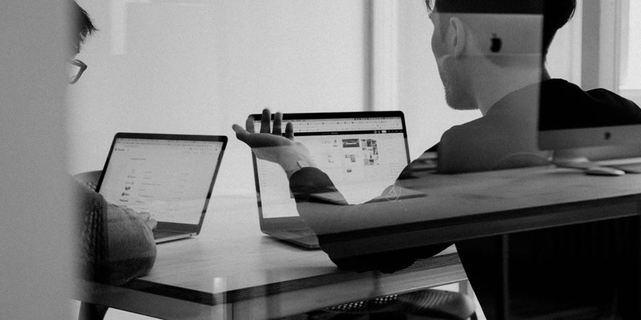 Two men with laptops seen through a pane of glass.